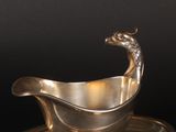 a silver gravy with a bird on it on a saucer