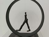 sculpture représentant un homme marchant à l'intérieur d'un objet circulaire posé sur une table