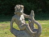 une statue représentant une sirène assise sur un rocher dans l'herbe
