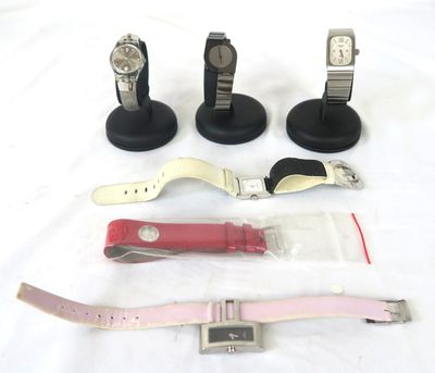 quatre montres et un présentoir à montres posés sur une surface blanche