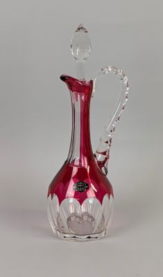 un vase en verre rouge muni d'une anse, posé sur une surface blanche