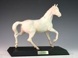 statue d'un cheval blanc au galop, posée sur un socle noir, sur fond gris