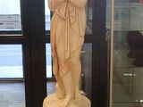 une statue représentant une femme debout sur un socle devant une porte vitrée