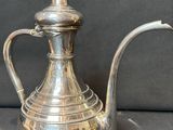 cafetière plaquée argent avec une anse incurvée sur fond noir