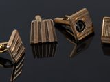 three gold cufflinks with black stones on a black surface
