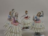three porcelain figurines of women in dresses and hats on a white surface