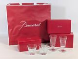 a red box with four glasses and a red bag with the word baccarat on it