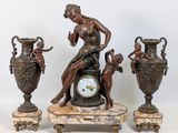 une statue représentant une femme assise sur une table, à côté de trois vases et d'une horloge