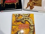 three books on a white table with a gold chair and a red chair
