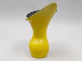 a yellow vase with a black top on a white surface