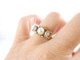 a woman ' s hand holding a pearl and diamond ring