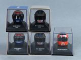 six casques de course miniatures présentés dans des vitrines posées sur une surface blanche