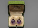 une photo d'une paire de boucles d'oreilles en verre violet dans une boîte verte