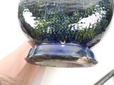 a hand holding a blue and green vase with a hole in it