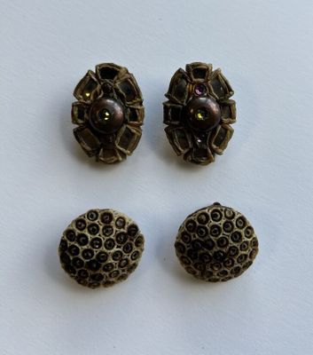 trois boutons anciens et une perle sont posés sur une surface blanche