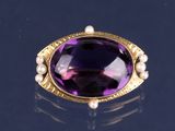 une photo d'une bague ornée d'une pierre violette et d'une perle, posée sur un fond noir