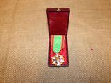 une boîte rouge ornée d'un ruban vert et d'une médaille en or