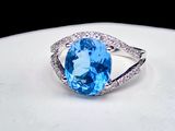 une bague ornée d'une topaze bleue ovale et de diamants, posée sur un fond blanc
