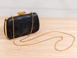 a black clutch bag with a gold chain on a wooden table
