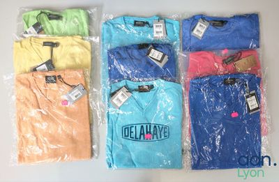 plusieurs t-shirts de différentes couleurs, dans des sacs en plastique, posés sur une surface blanche