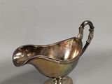 an antique silver plated sauce boat with a handle on a stand