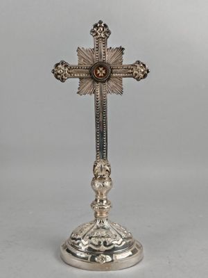 une croix en argent posée sur un socle, avec une pierre rouge au centre
