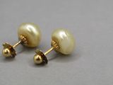 une paire de boucles d'oreilles en perles et en or posées sur un fond gris