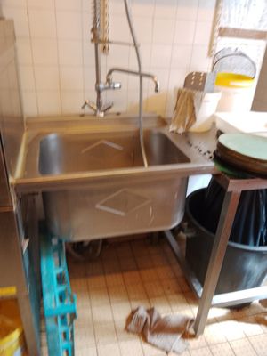 un évier au milieu d'une cuisine, avec une poubelle posée par terre