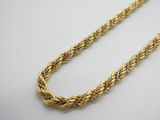 un gros plan d'un collier à maillons dorés posé sur une surface blanche
