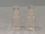 une paire de flacons de parfum en verre transparent avec des bouchons transparents, posés sur une surface blanche