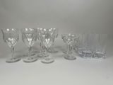 six verres à vin en cristal et un gobelet en verre posés sur un plan de travail blanc