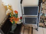 a metal step stool next to a vase of flowers on a tiled floor