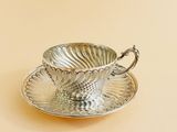 a silver cup and saucer sitting on a saucer