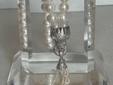 un collier de perles blanches muni d'un fermoir en argent, présenté sur un support transparent