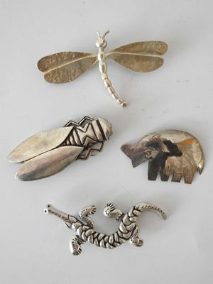 three silver brooches, a dragonfly, a tiger, and a dragonfly