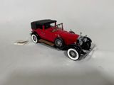 une petite voiture rouge avec un toit noir posée sur une surface blanche