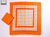 une écharpe carrée orange et blanche, ornée de boules blanches