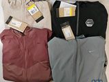 trois paires de vestes Nike et un sac de vêtements posés sur une surface blanche
