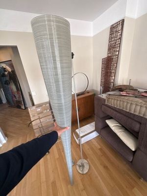une personne debout dans une pièce où se trouvent un lit et un lampadaire