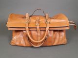 brown leather handbag sitting on a gray surface with a black suitcase