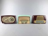 three old fashioned radio ' s are lined up on a table