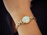 woman wearing a gold watch with a white dial on her wrist