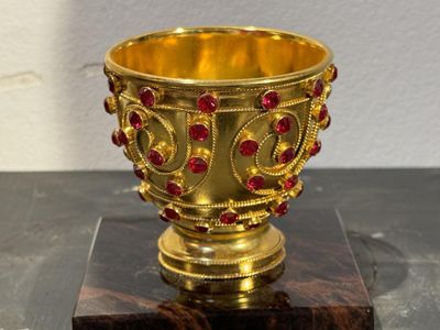 une coupe en or ornée de pierres précieuses rouges, posée sur un socle en bois