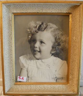 une vieille photo d'une petite fille en robe blanche, dans un cadre doré