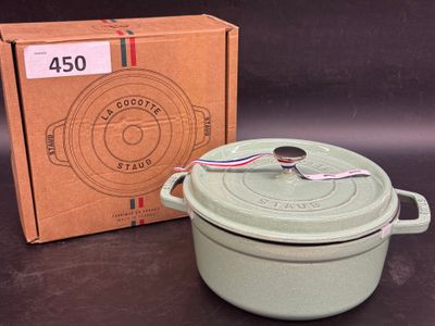 un plat à gratin vert avec couvercle, dans sa boîte, posé sur la table à côté d'un carton
