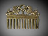 brass hair comb with two lions on it and a key in the middle of the comb