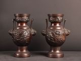 une paire de vases anciens en bronze posés sur une table, sur fond gris