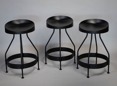 trois tabourets noirs placés les uns à côté des autres sur une surface blanche