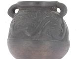 a black vase with a design on it on a white surface