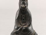 une statue noire représentant une femme assise sur une surface blanche
